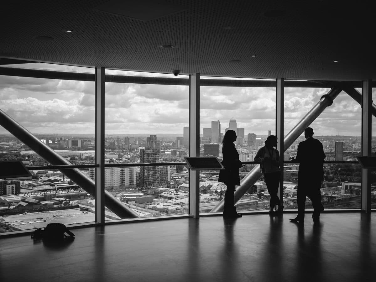 Three executives talking at a high floor window above a city skyline