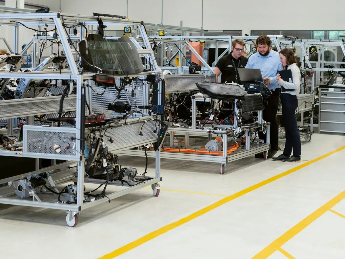 Three colleagues reviewing work at a laptop on an engineering assembly floor